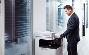 Photo of a man using a PalmSecure scanner to log into a photocopier in an office. 