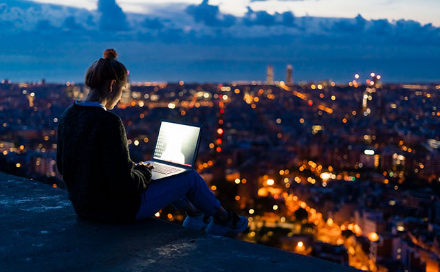 Woman using laptop at dawn above the city, Barcelona, Spain