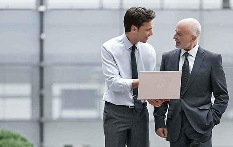 Two men discussing while holding laptop