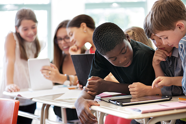 A row of desk with students working on tablet computers