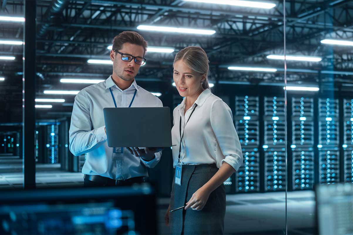 IT specialist and female IT specialist in the data centre looking at a laptop