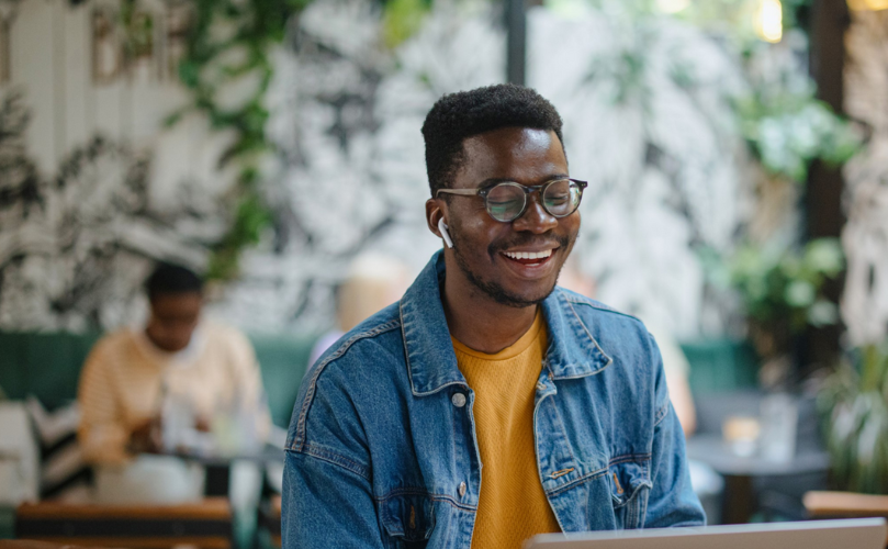 A person sitting at a table with a computer and smiling