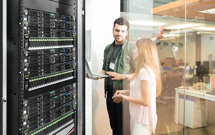 Two individuals standing near a server rack, managing and maintaining the network infrastructure.