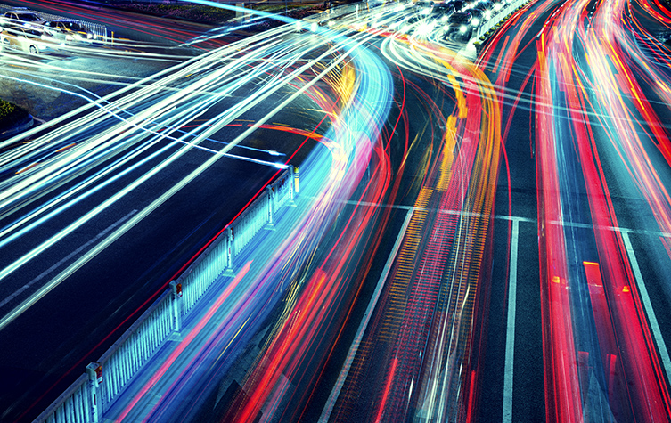 A bustling city street filled with cars and illuminated by vibrant lights.