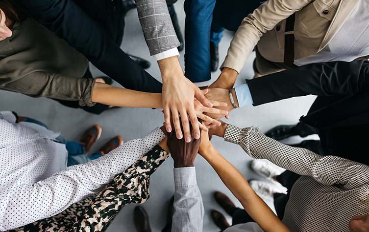 A diverse group of professionals in formal attire, standing together and joining hands in unity.
