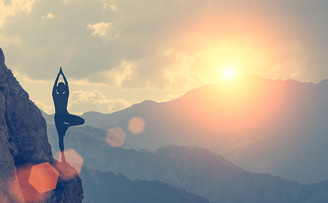 Photo of a person doing yoga on a mountain, with clouds and sunset in the background. 