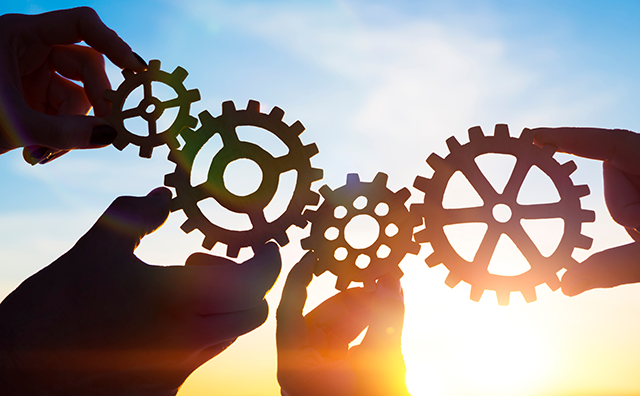 Photo of hands holding cogs together with a sunset behind