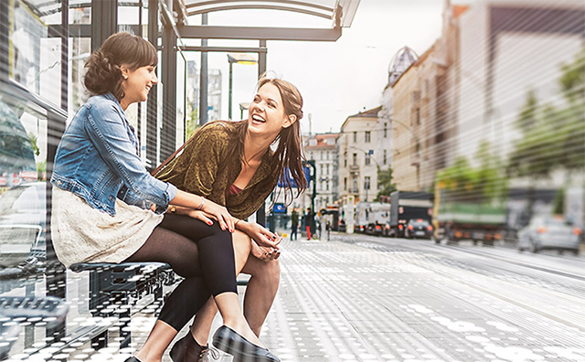 Photo of two women smiling and talking at a bus stop