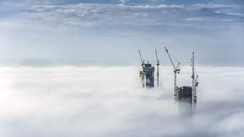 Photo of construction cranes and buildings visible above the clouds