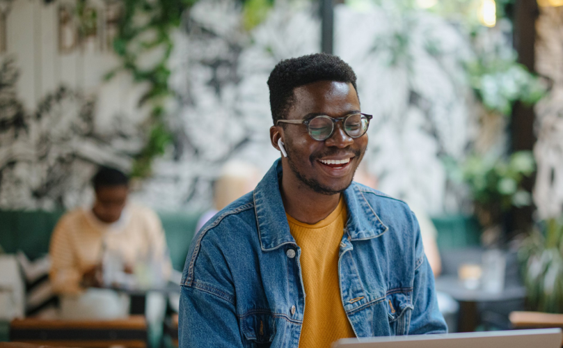 A person sitting at a table with a computer and smiling 