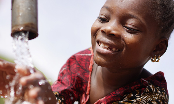 Smiling young girl with her hands under a running tap.