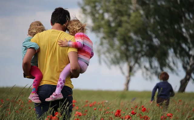 Man walking through field holding children