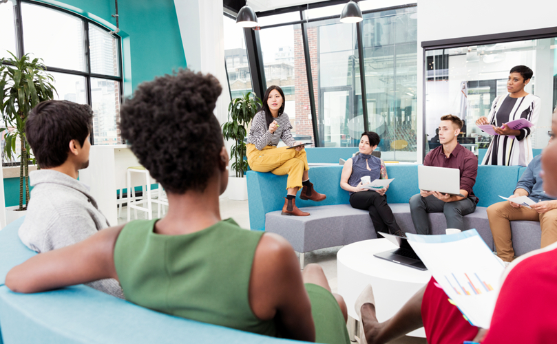 A diverse group sitting in a meeting, reviewing a project and brainstorming ideas they are working together on.
