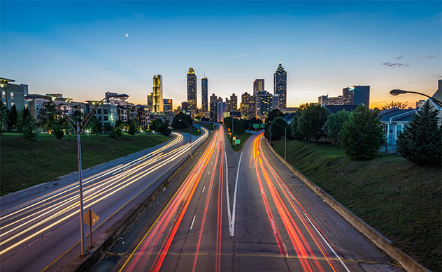Motion-blur photo of traffic on roads in front of Atlanta, USA, skyline.