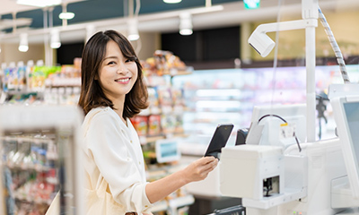 スーパーでの買い物でスマートフォンで支払いを行う女性の画像。