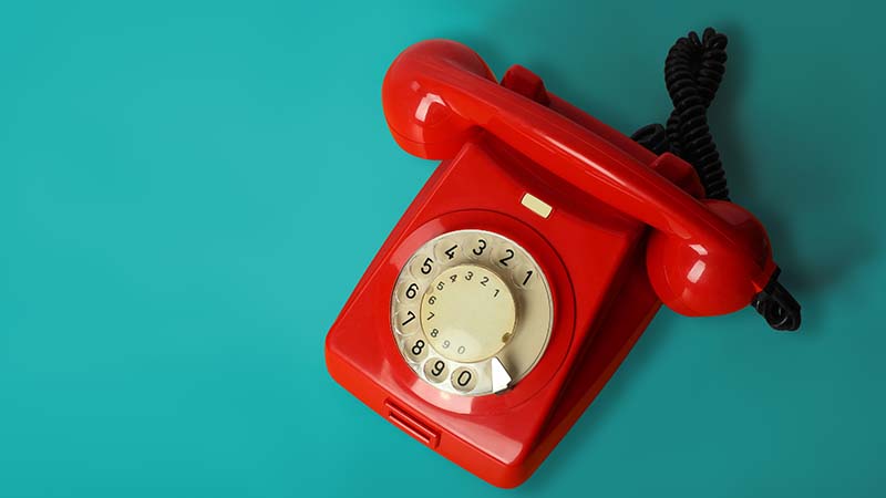 Photograph of an old-fashioned red dial telephone on a blue background