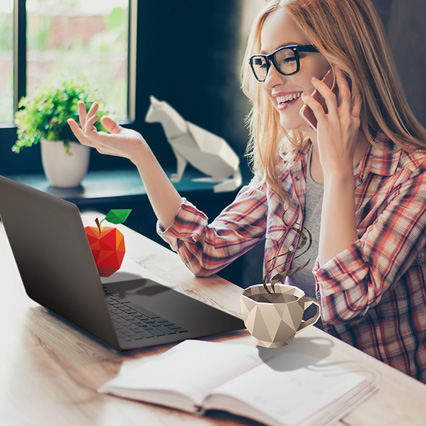 woman talking on phone using laptop next to origami apple and coffee