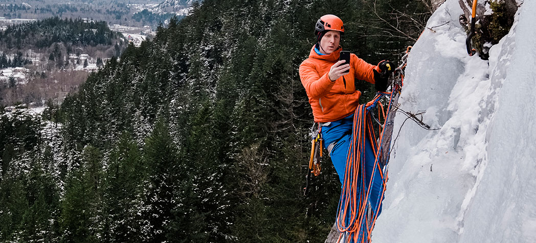 A mountain climber using a phone while on side of snowy mountain face