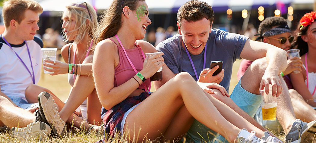 Young people partying outside in a field drinking and using a phone