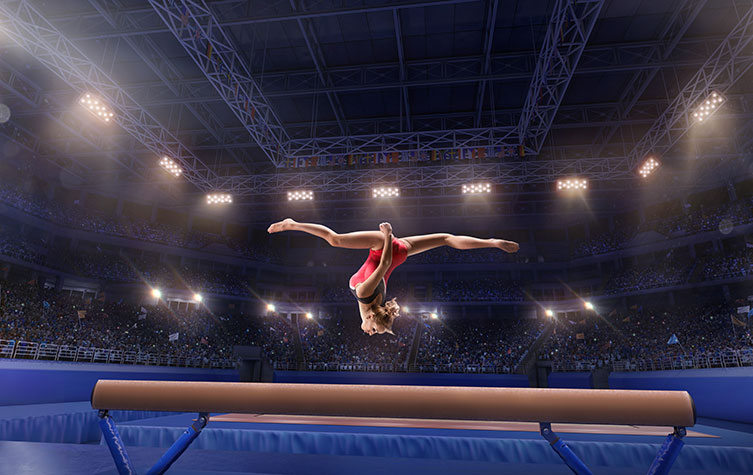 Female athlete doing a trick on gymnastics balance beam in a professional gym 